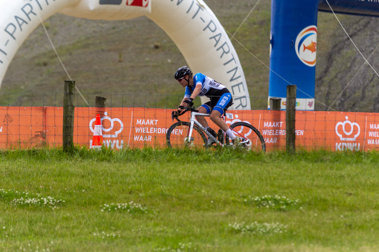 A woman in a cycling race sponsored by NK Dames, Wielrennen, and Junioren Dames.