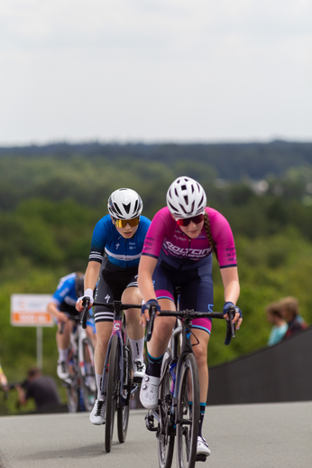 Two female cyclists are wearing helmets as they race along a street.