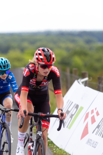 A woman in a black and red cycling outfit is riding her bicycle.