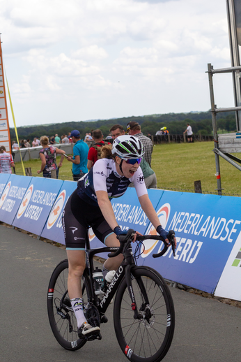 A woman racing on a bike wearing a black and blue outfit sponsored by NK Dames.