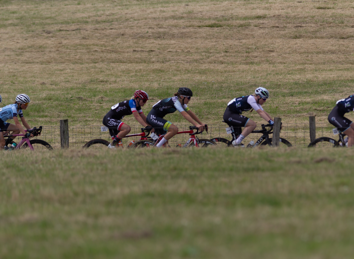 A group of cyclists racing with one wearing a jersey that says NK Dames.