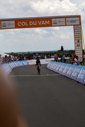 A cyclist wears a black shirt while riding along a race course.