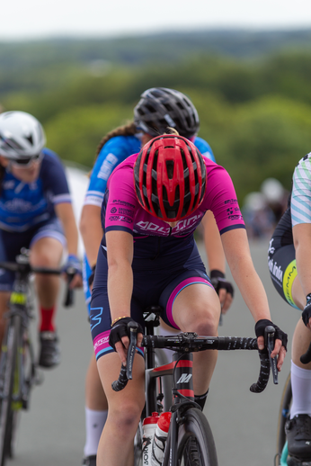 A female cyclist with a black and pink shirt is riding on the road.