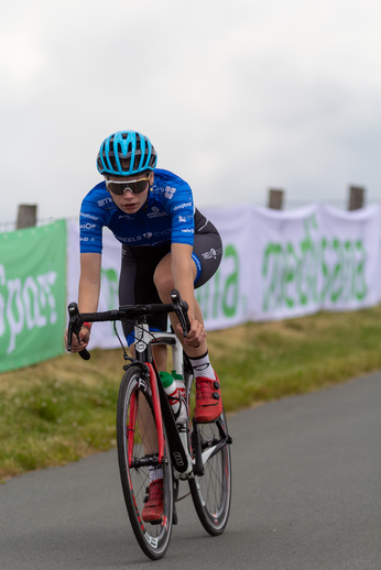 A young person on a red bike with the word "Junioren Dames" on their blue shirt.