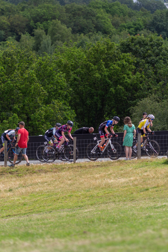 A group of cyclists on a path, one wearing a pink top and another wearing a blue top.