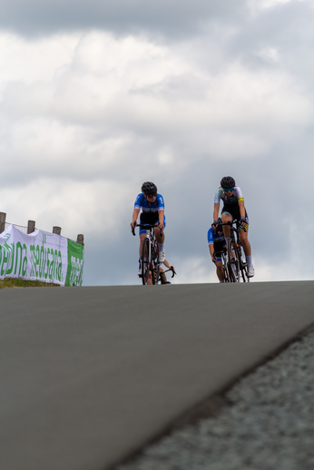 Two cyclists wearing blue shirts and helmets are riding up a hill.