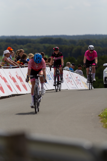 A woman in a pink shirt and black helmet is riding a bike on the road.