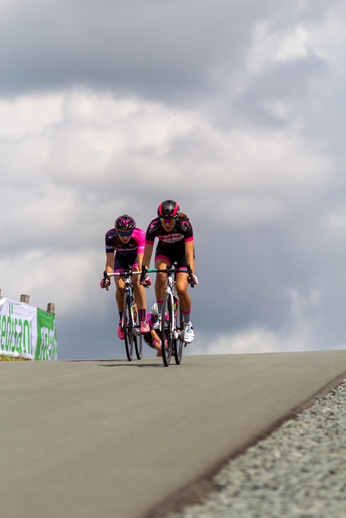 Two cyclists riding on a road with one wearing a pink jersey.