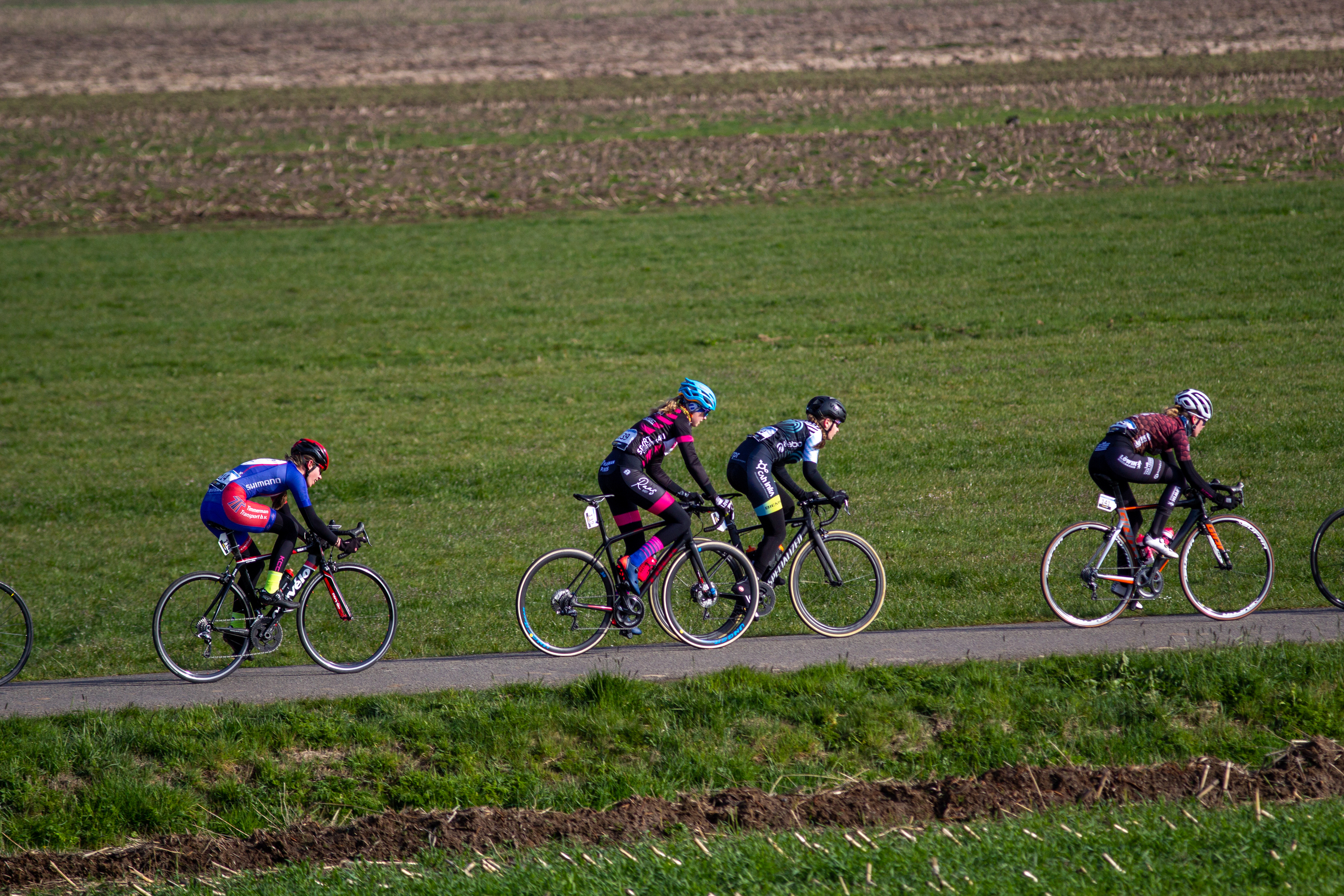 A group of cyclists wearing helmets ride on a paved road.