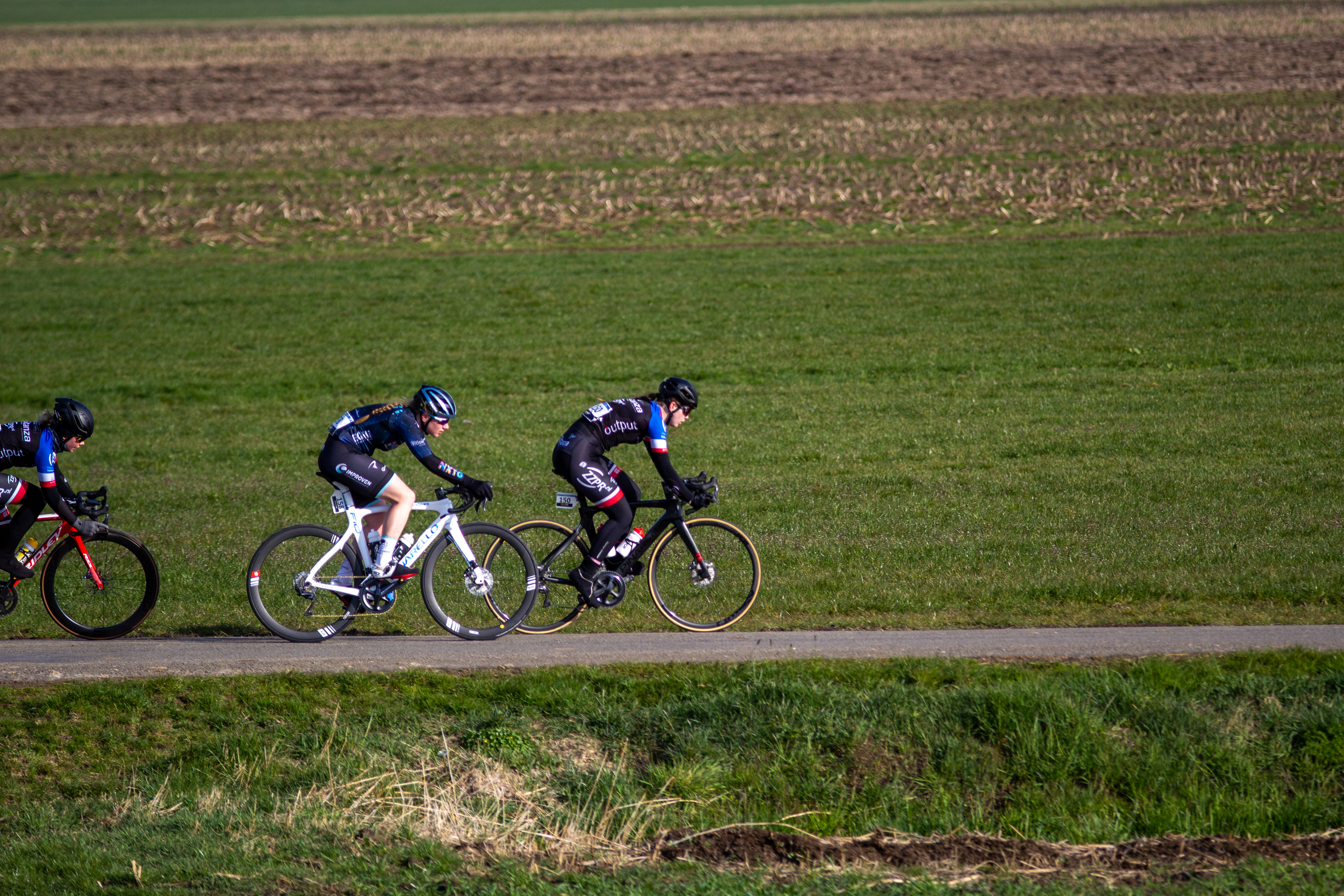 Three cyclists are riding side by side on a road in the Netherlands.