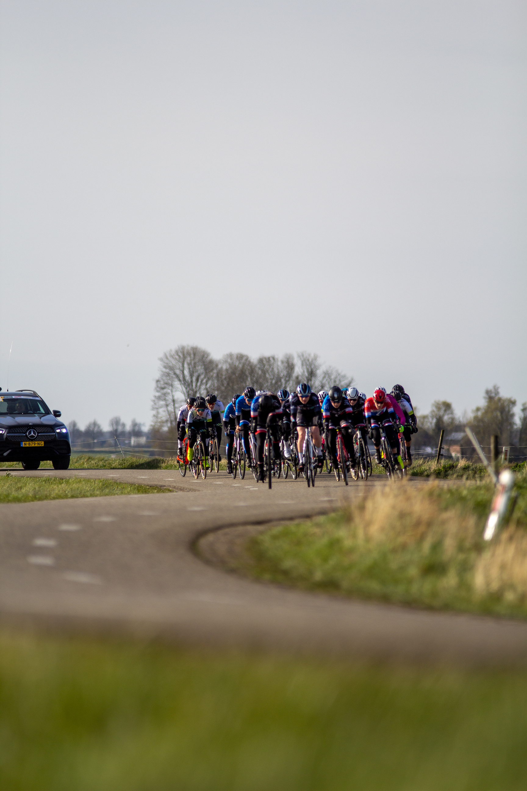 Group of cyclists riding on a road, the cyclist in front wears a pink shirt and black helmet.