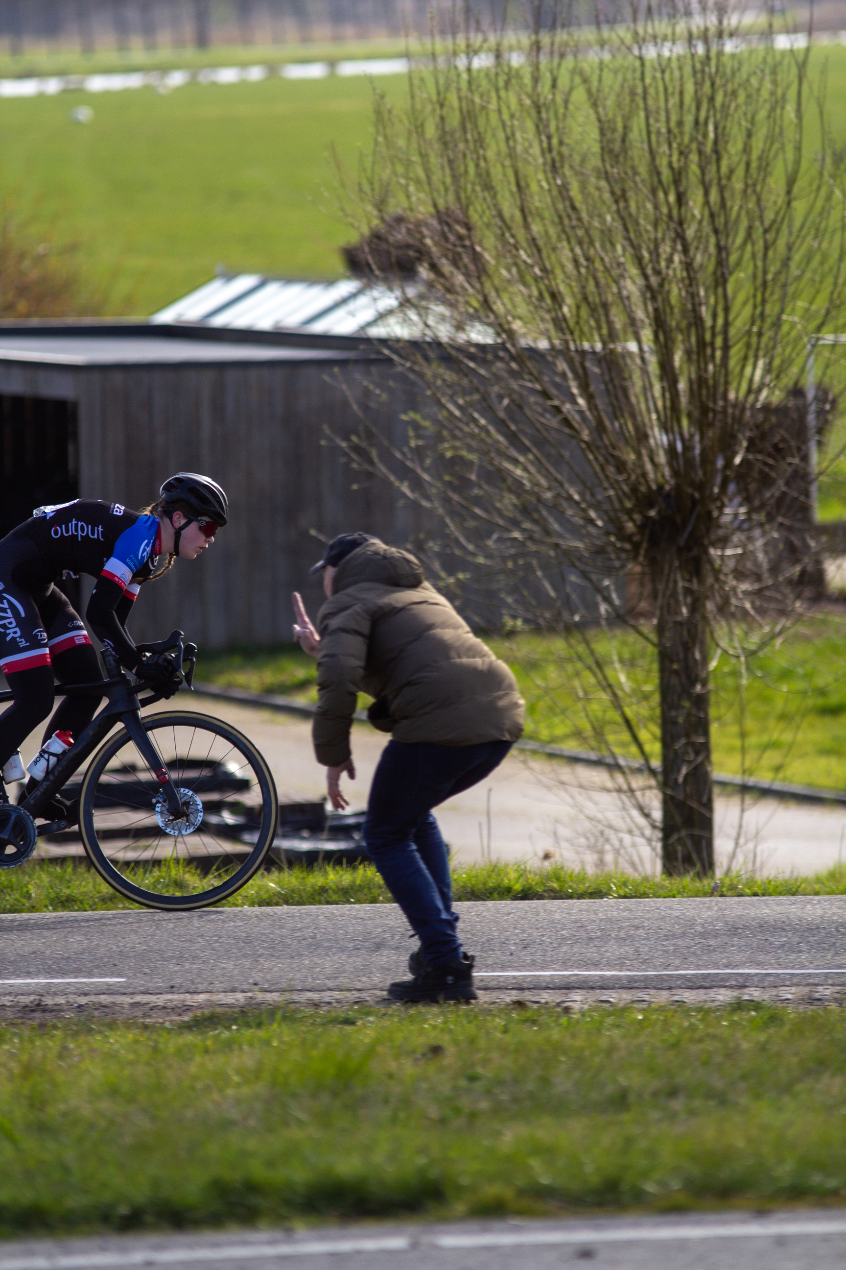 Two people riding bikes, with one wearing a black shirt that says "Wielen".