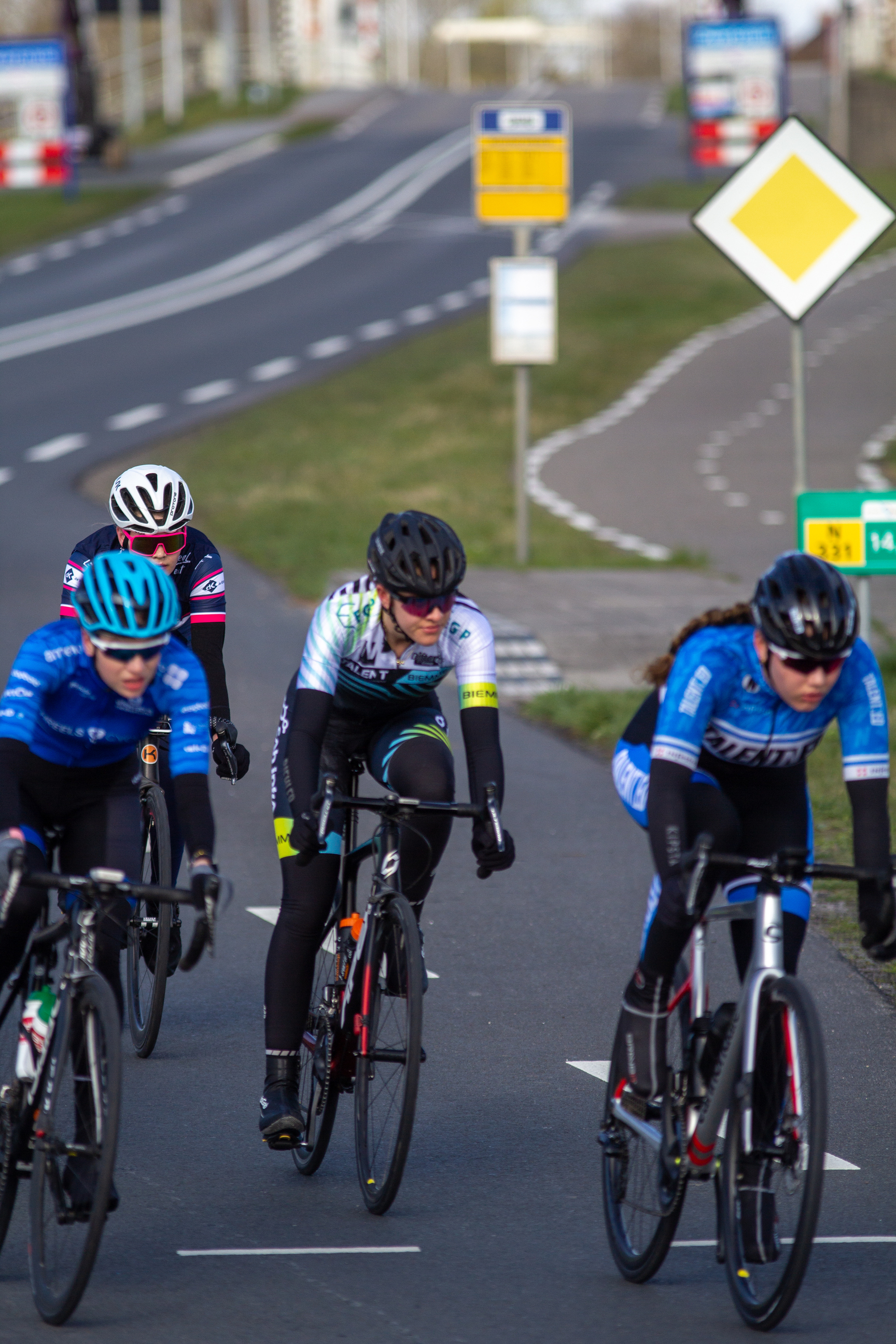 A group of cyclists racing on a road with one cyclist ahead.