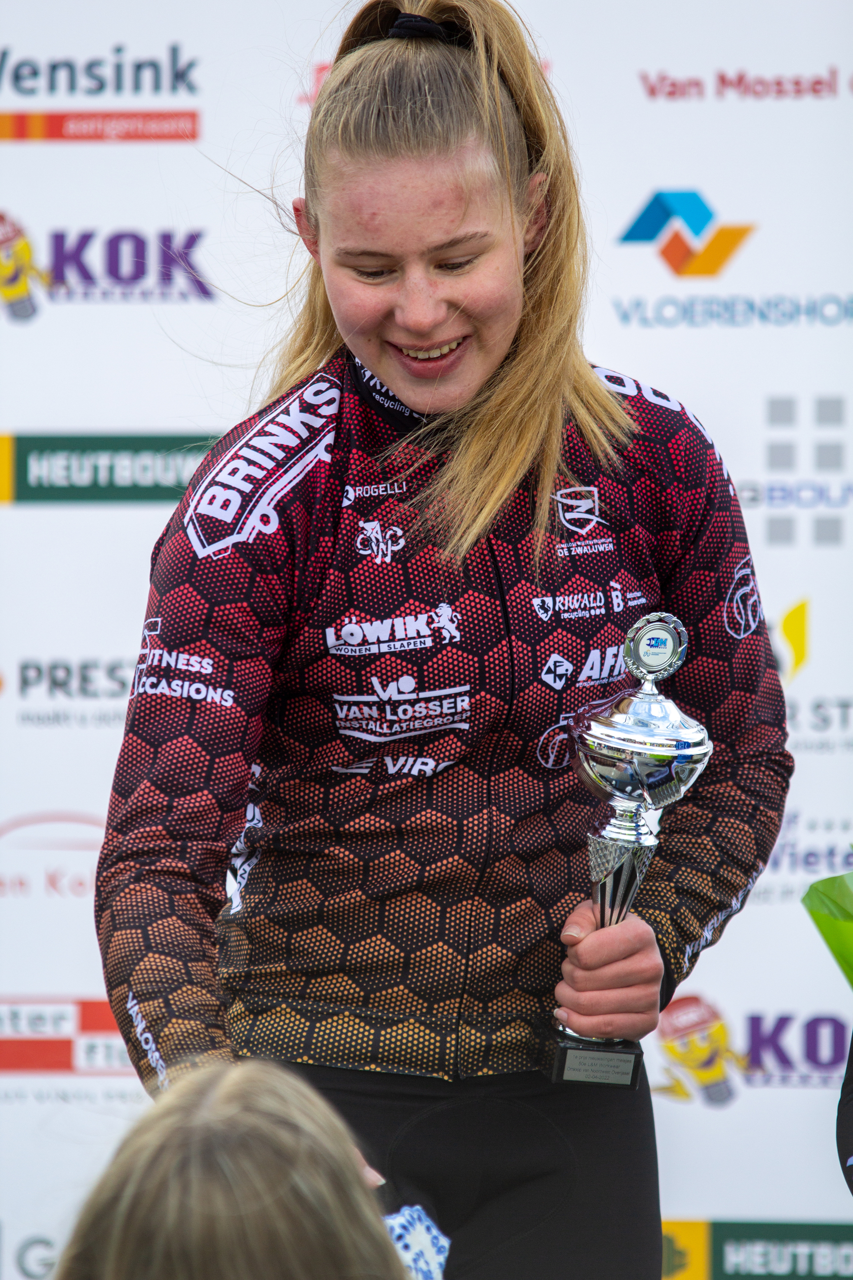 A blonde woman in a maroon and black dress holding a trophy.