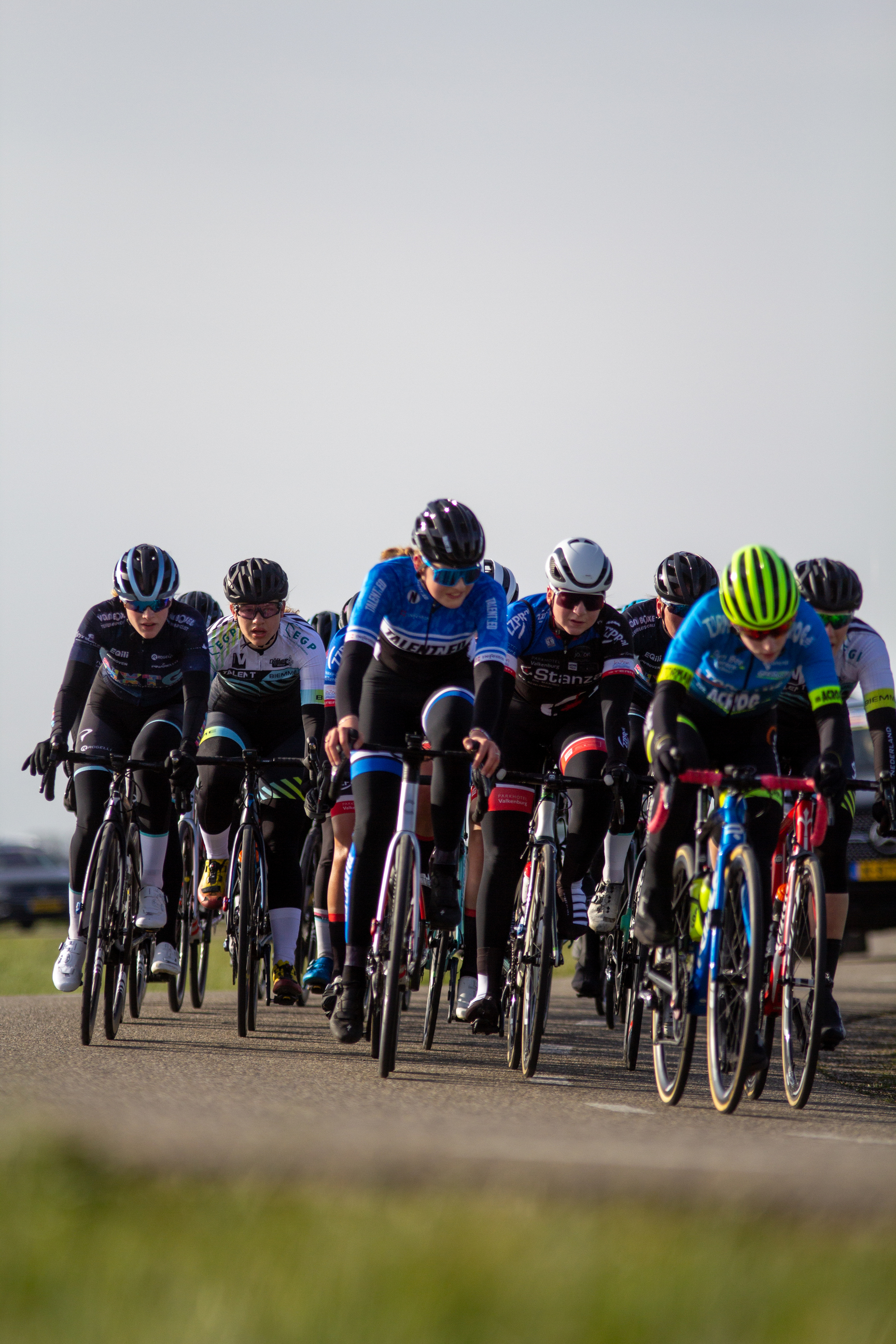 A group of cyclists wearing helmets and riding on a paved road in a grassy field.