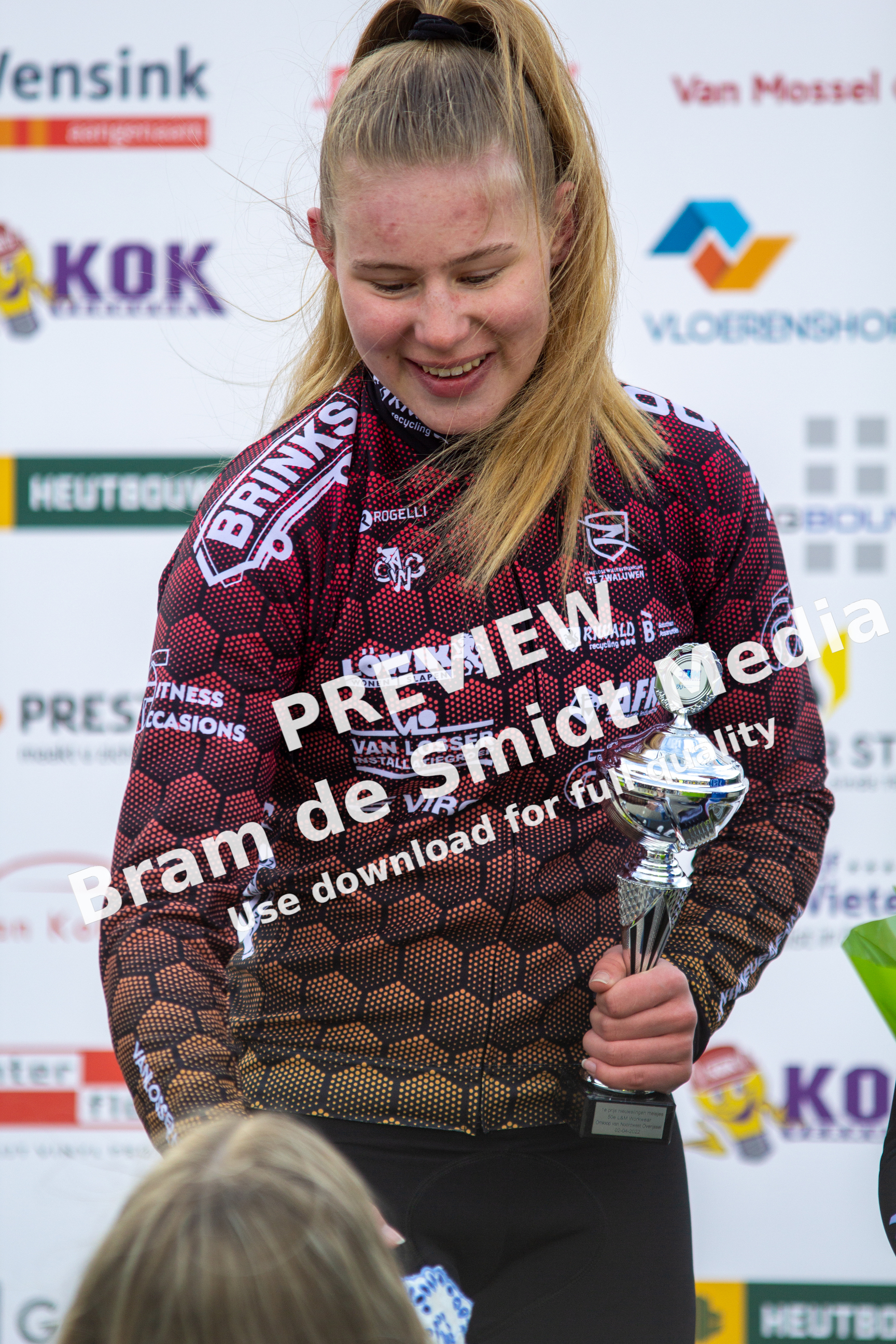 A blonde woman in a maroon and black dress holding a trophy.