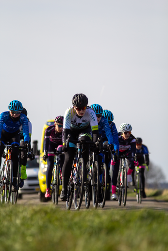 A group of cyclists wearing helmets race down the road.