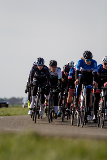 Women in a bike race wearing blue shirts sponsored by Wielrennen.