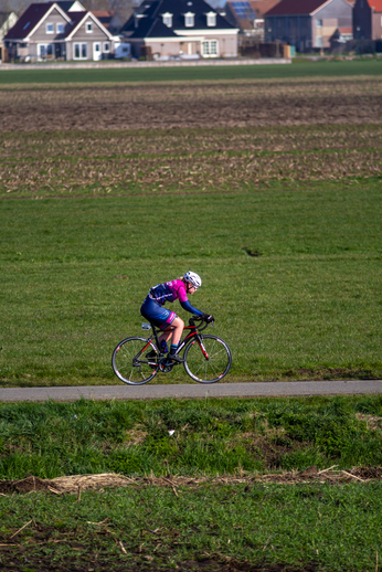 A cyclist wears a helmet and rides through an open field.