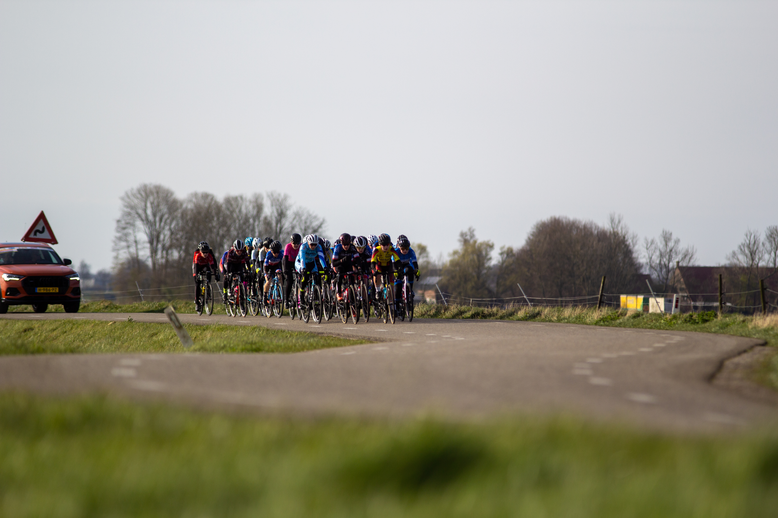 A group of cyclists racing on a road with the name Noord West Overijssel Dames.