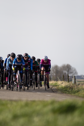 A group of cyclists on a road with one in the lead, wearing a red jersey.