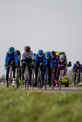 A group of cyclists riding on the road in front of a truck with yellow writing.