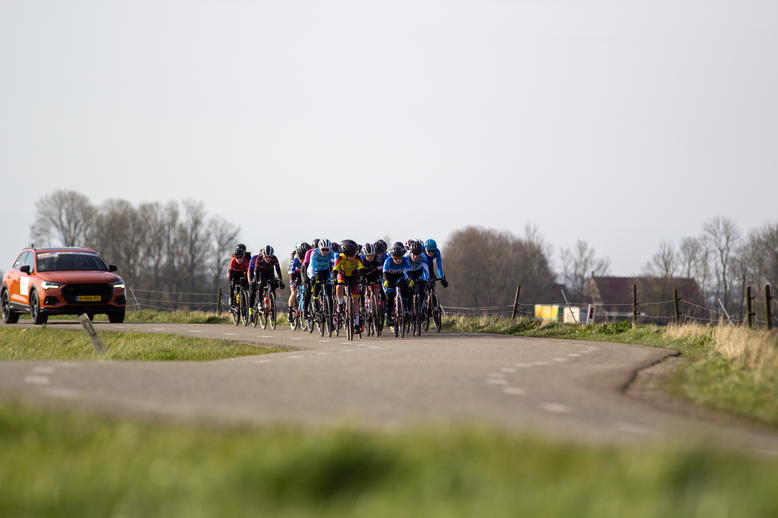 A group of cyclists riding on a road with the words Noord West Overijssel dames above them.