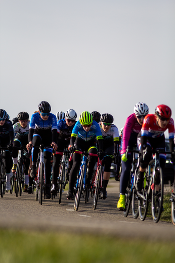 Women cycling in a race, wearing helmets and wearing blue and black and red jerseys.