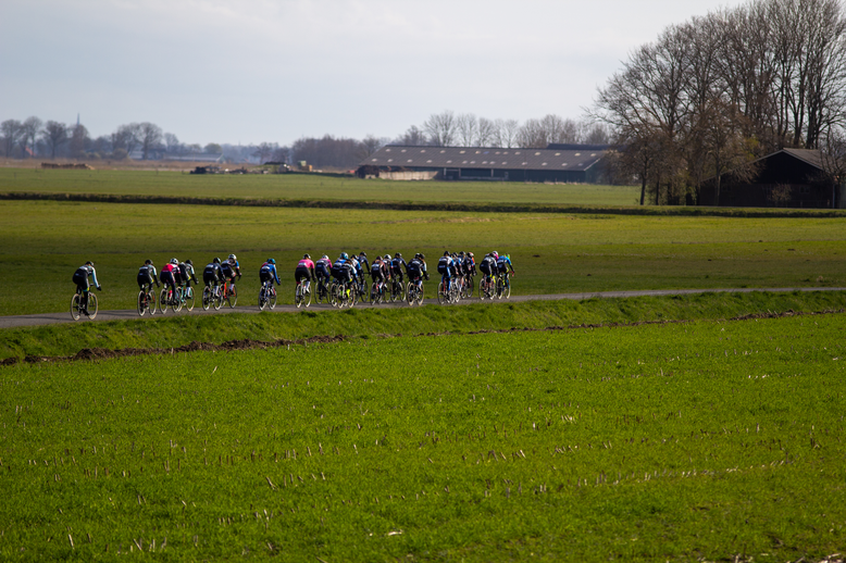 A group of cyclists are riding in a line on a grassy field, with the word "Wielrennen" displayed above them.