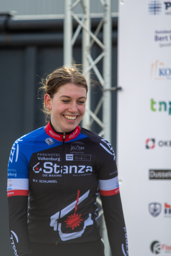 A woman in a blue and black cycling jersey is smiling for the camera at Wielrennen, Noord West Overijssel Dames.