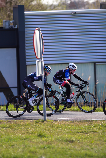 Two cyclists are racing on a street. They wear helmets and jerseys with numbers 15, 16 and 17.