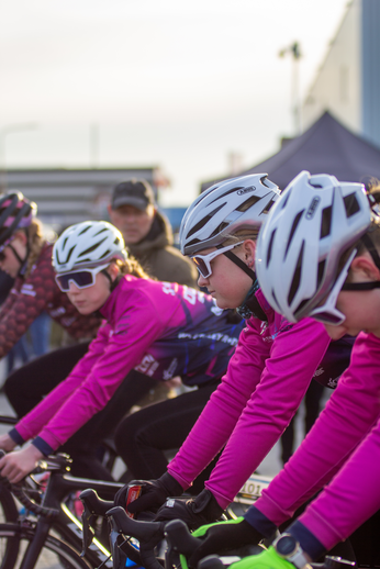 Four cyclists wearing pink jerseys are riding through a city street.