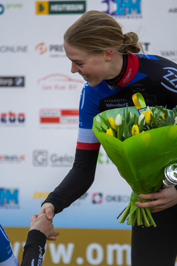 A woman presents a bouquet of flowers to another. They are both at the Noord West Overijssel Dames event in 2022.