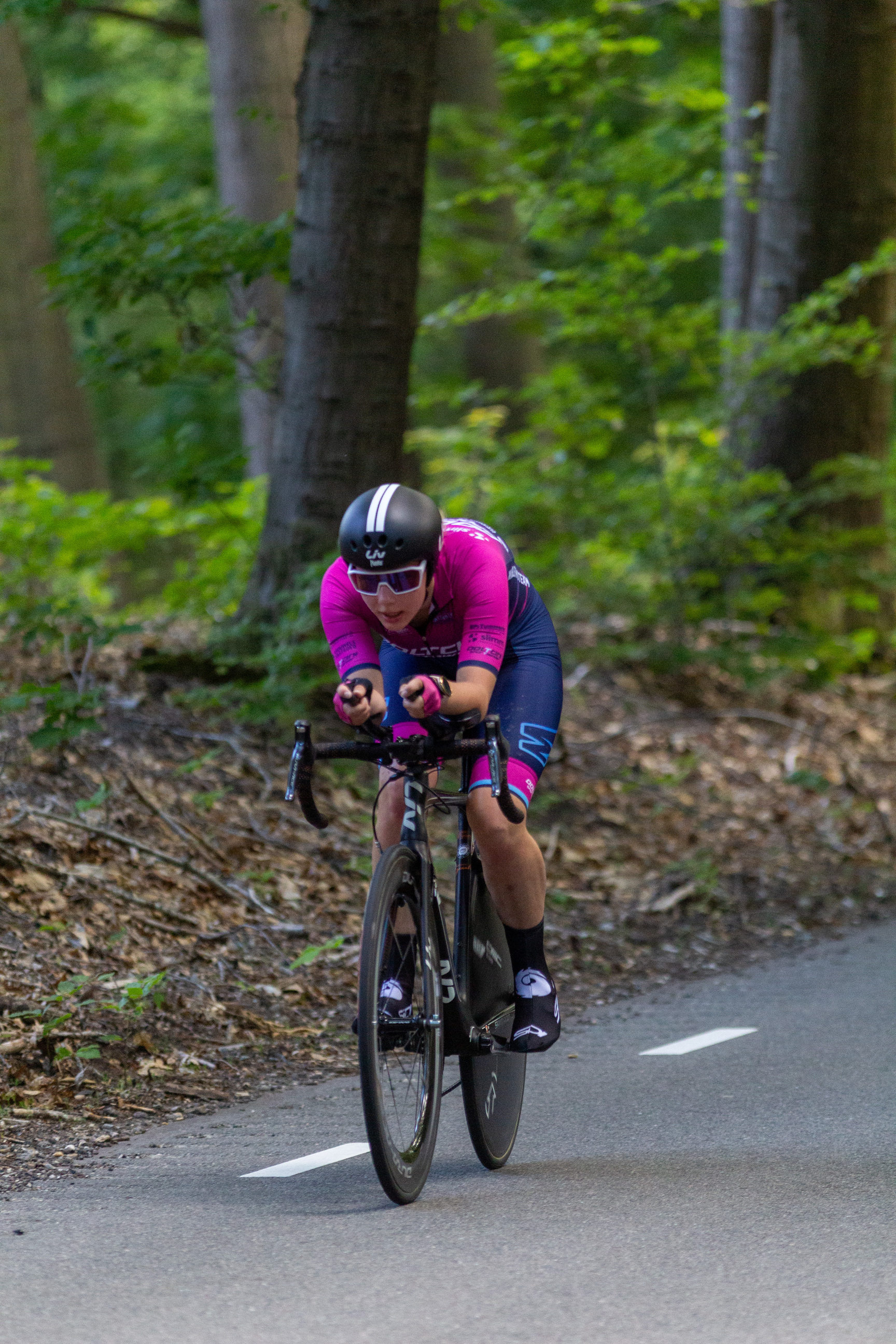 A cyclist dressed in pink jersey and blue pants is on the track with a bicycle.