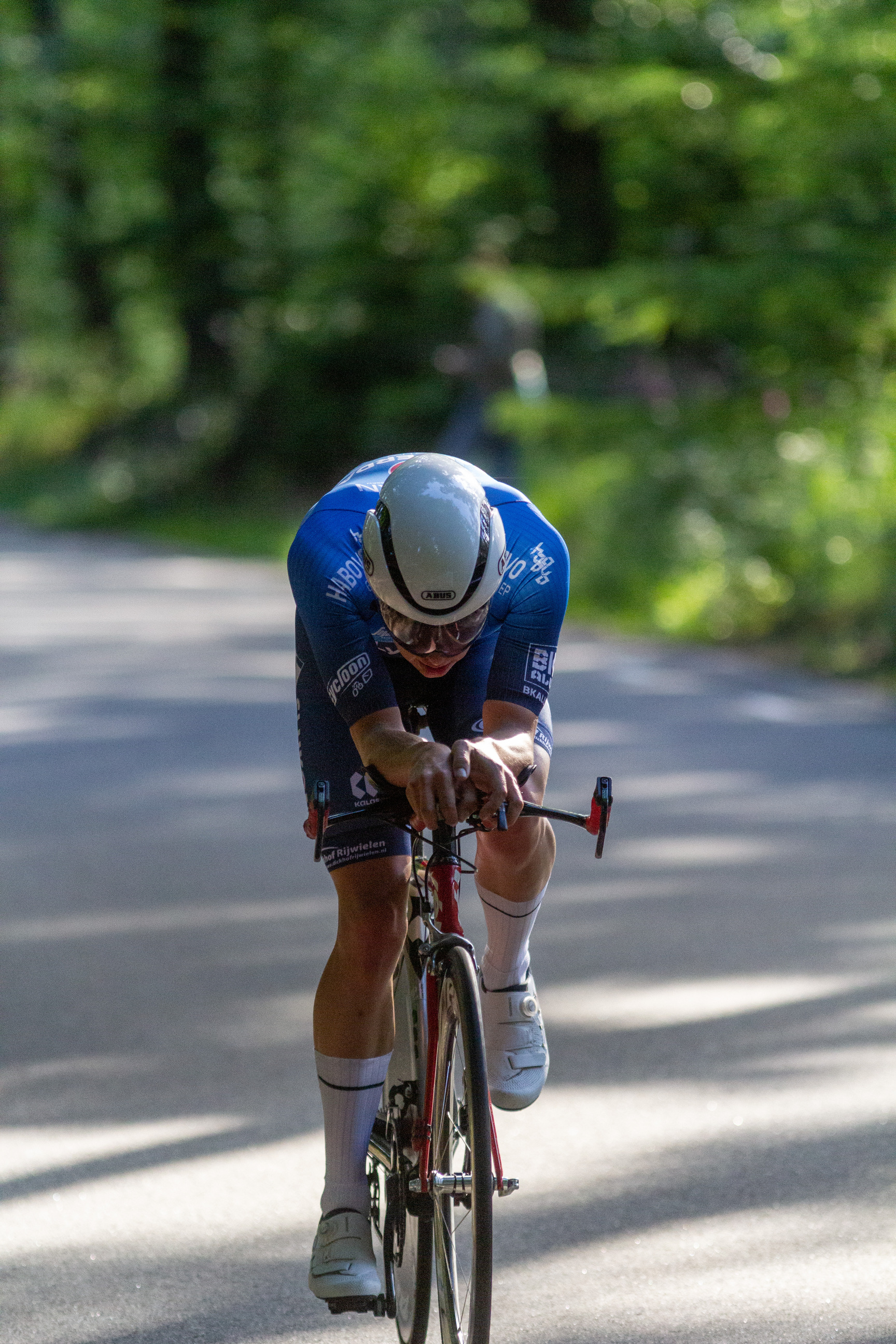 A man wearing a white helmet riding a bike on a road with trees in the background.