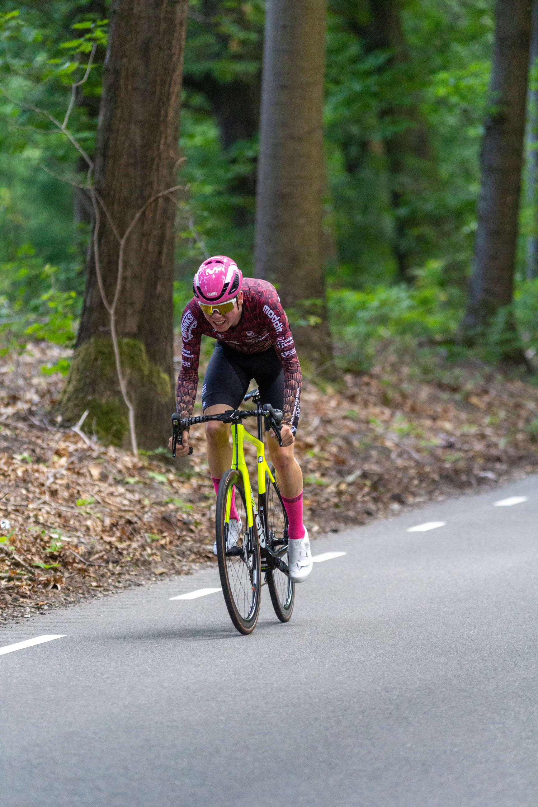 A female cyclist is wearing a pink helmet and riding a yellow bike.