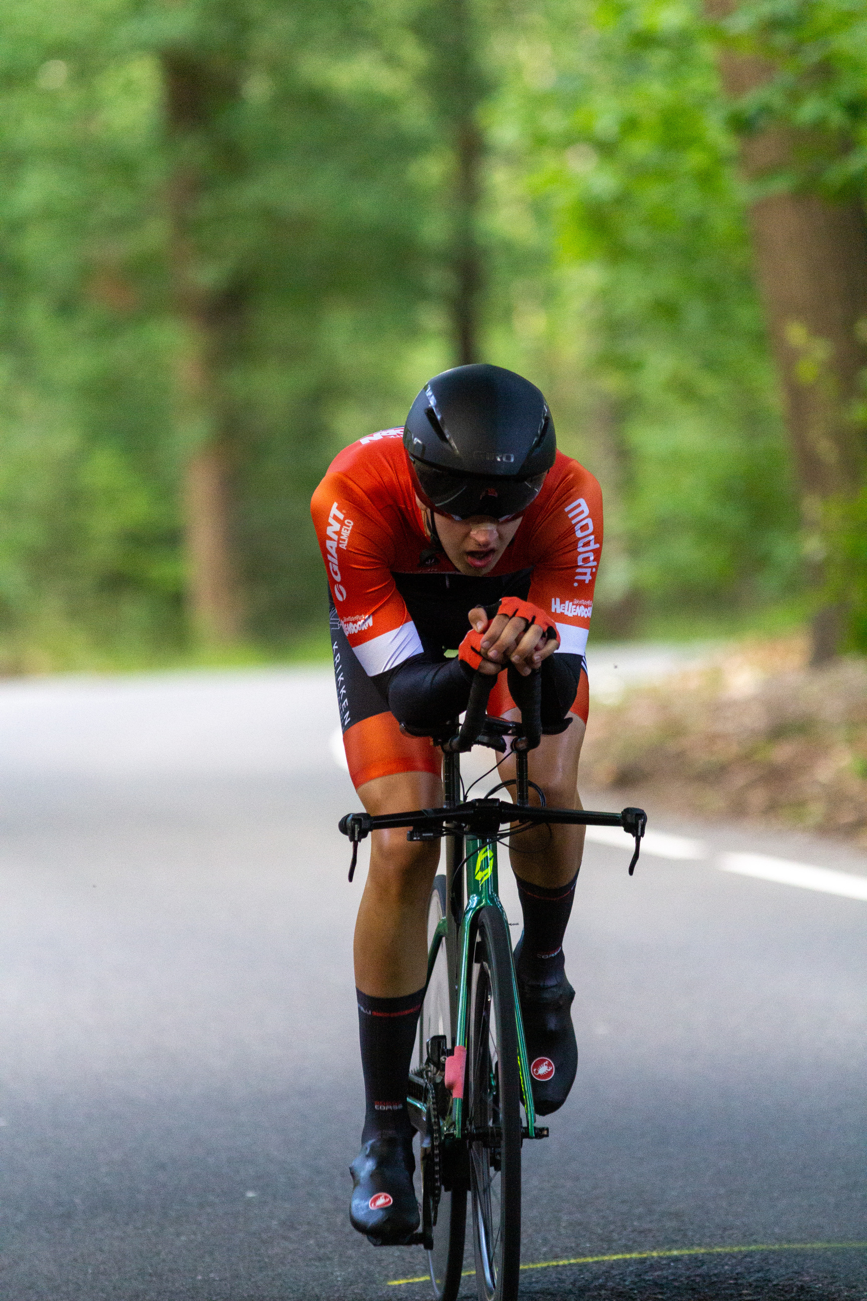 A man in a red Wielrennen jersey rides a green bike.