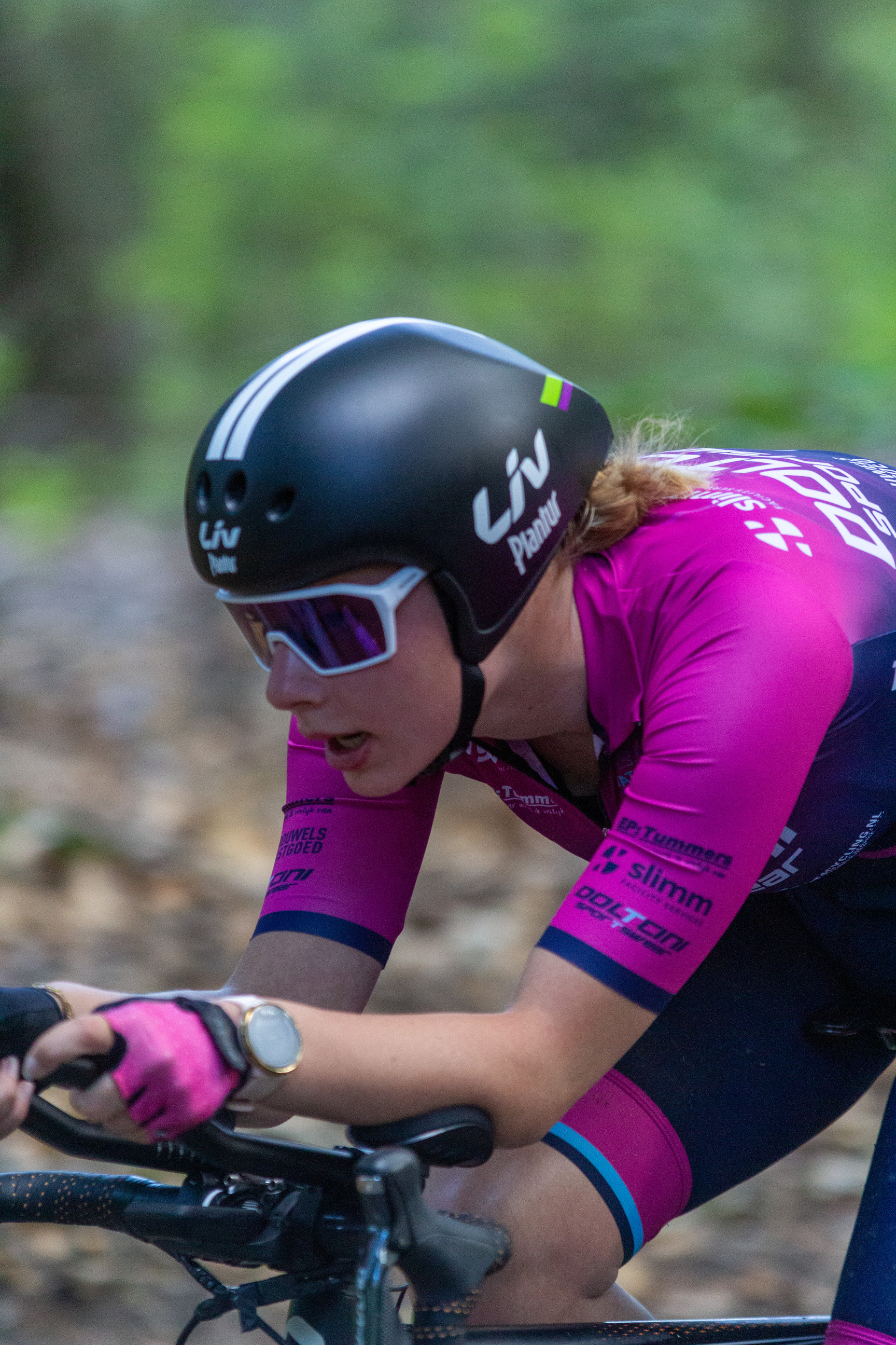 A woman is riding a bicycle with the words "Wielrennen" on her shirt and helmet.