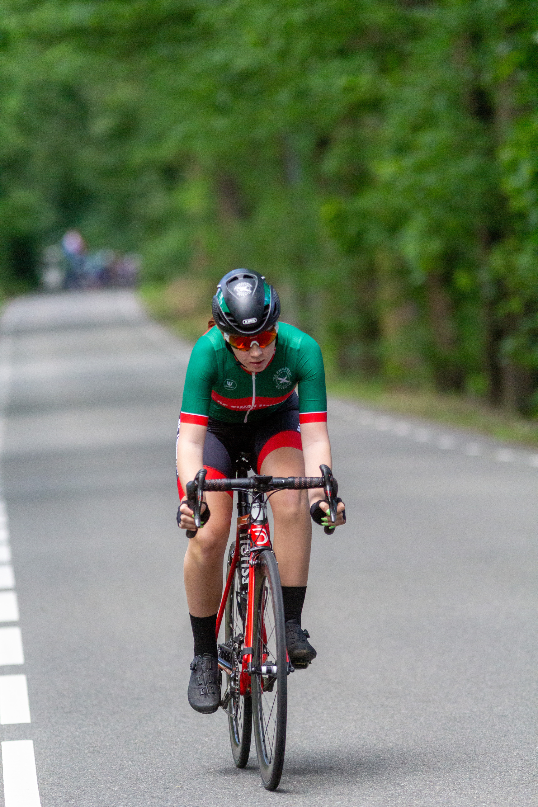 A man in a green and black jersey is riding a bike down the street.