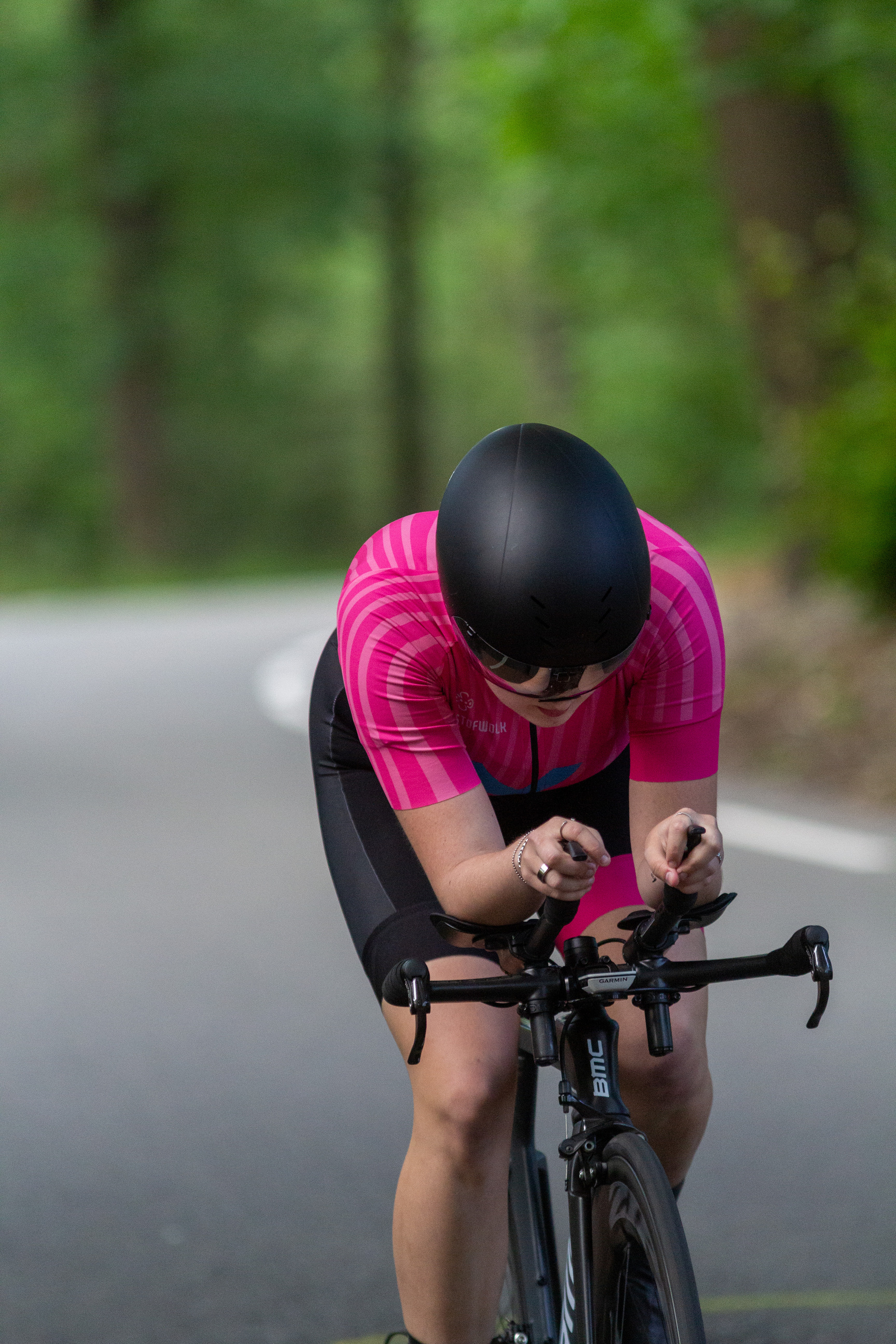 A girl is riding a black bike down a country road with trees in the background.