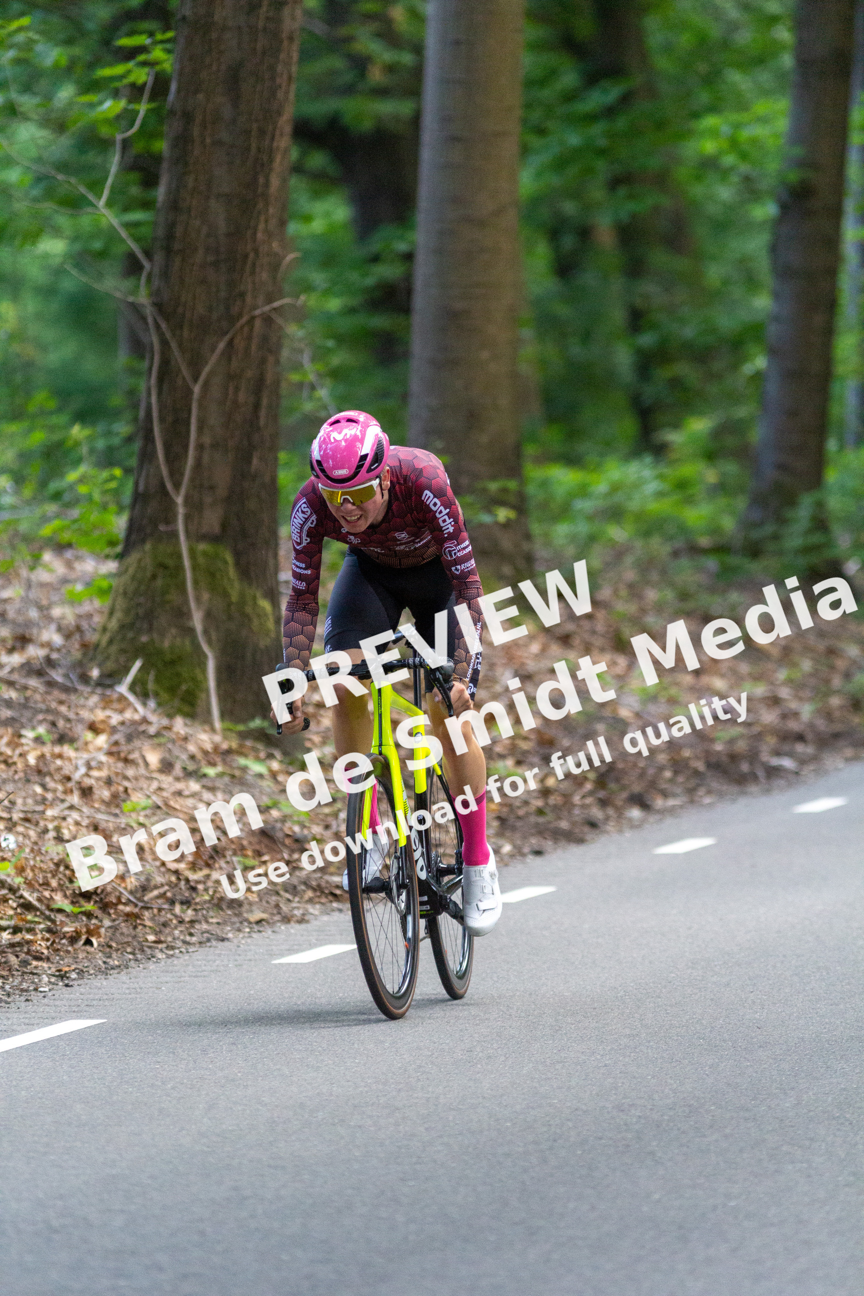 A female cyclist is wearing a pink helmet and riding a yellow bike.