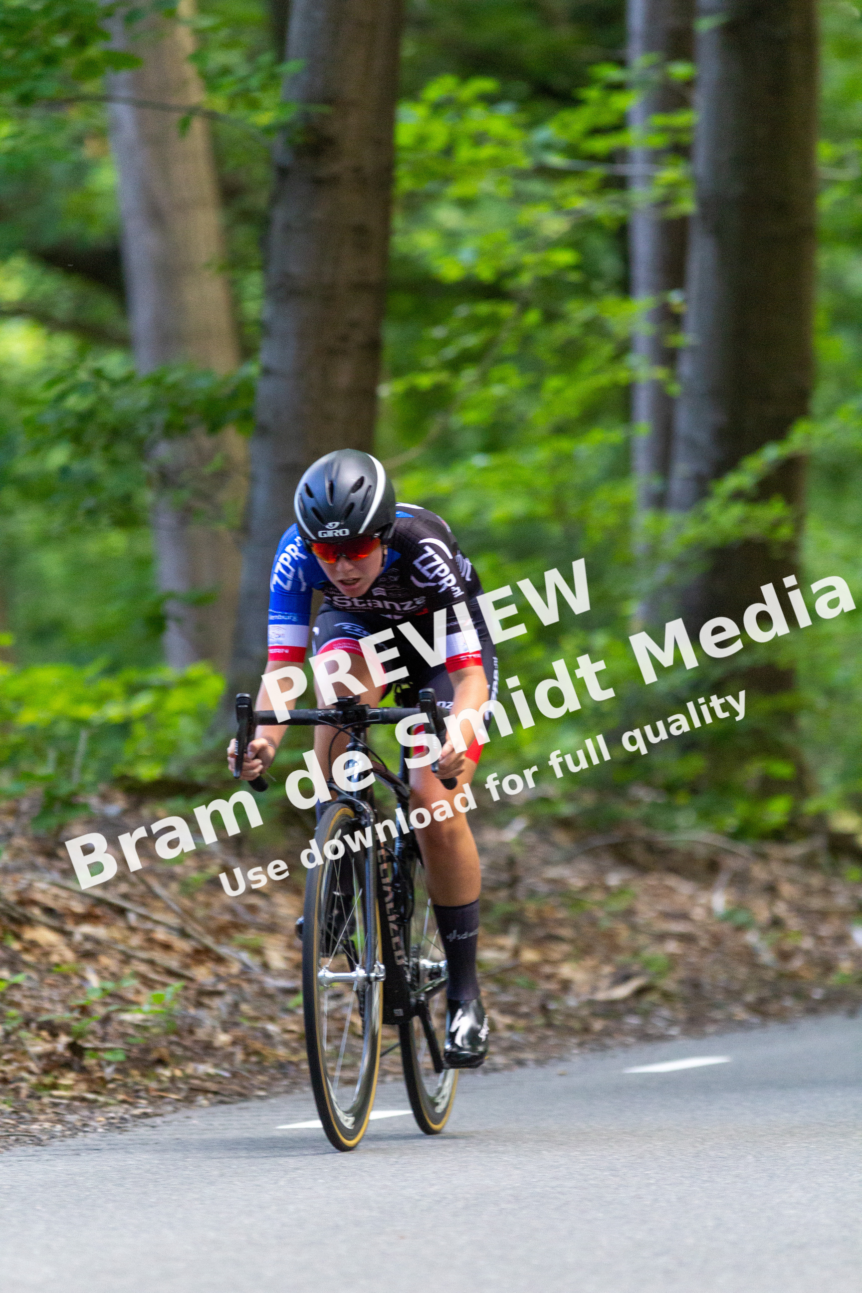 A cyclist on a trail wears a DK helmet and races wearing a blue, white and red outfit.