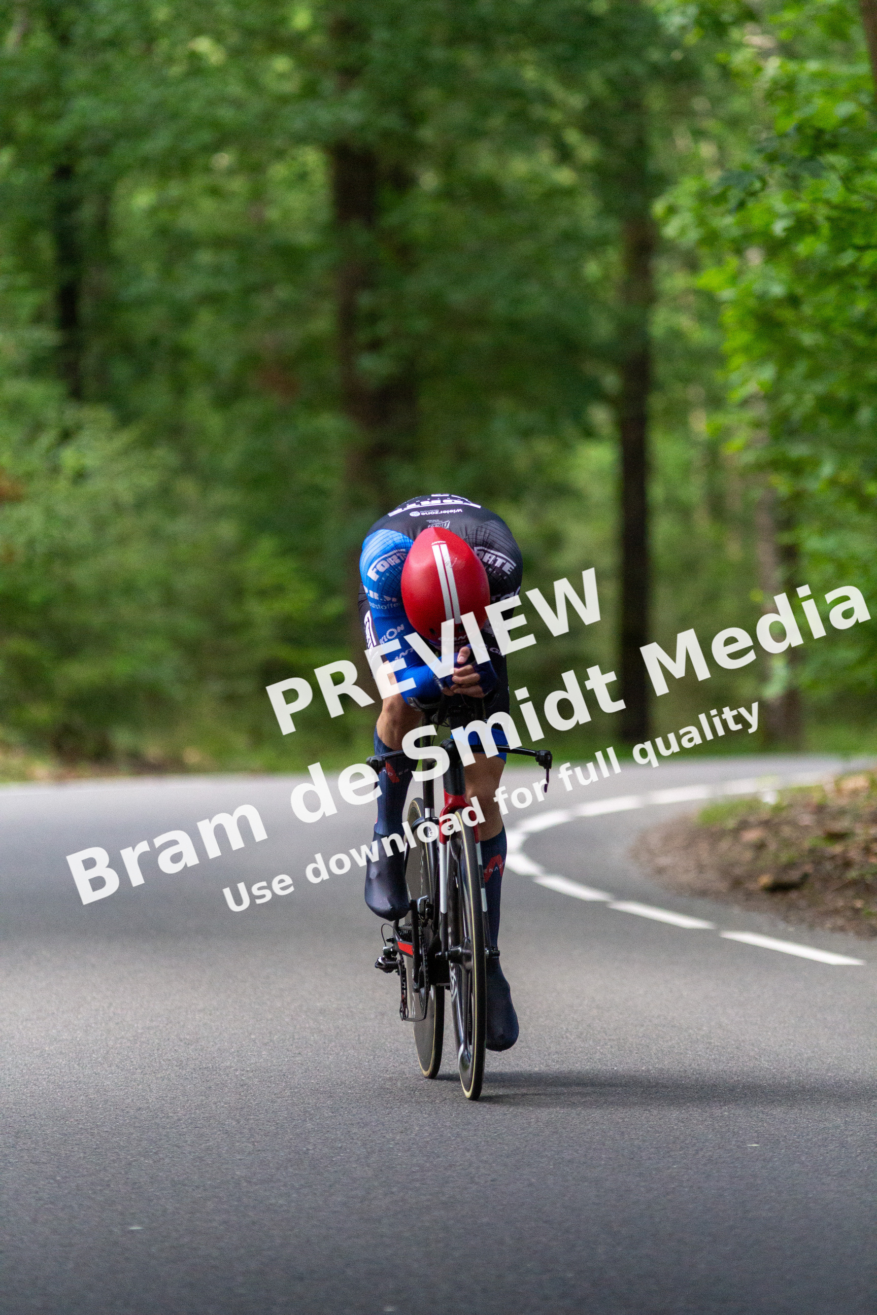 A man wearing a blue shirt and helmet rides his bicycle on the side of a road.