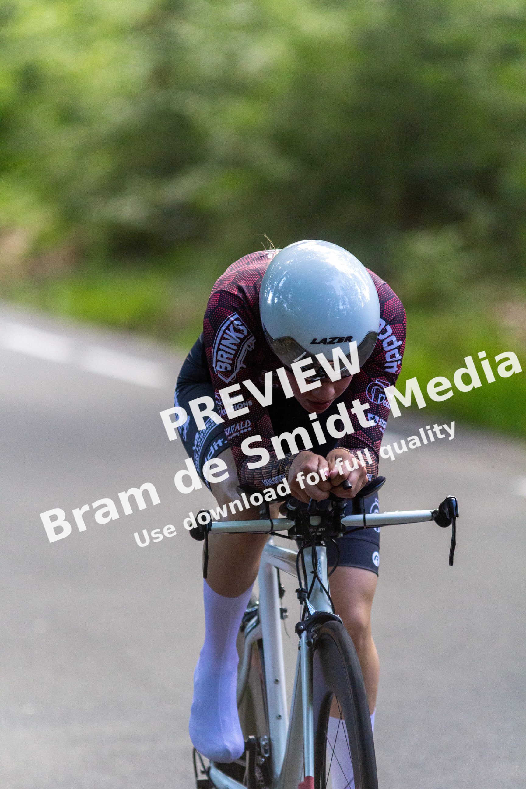 A man is riding a bike in the street. He has red and black on his shirt, a white helmet that says "Giant", and white socks.