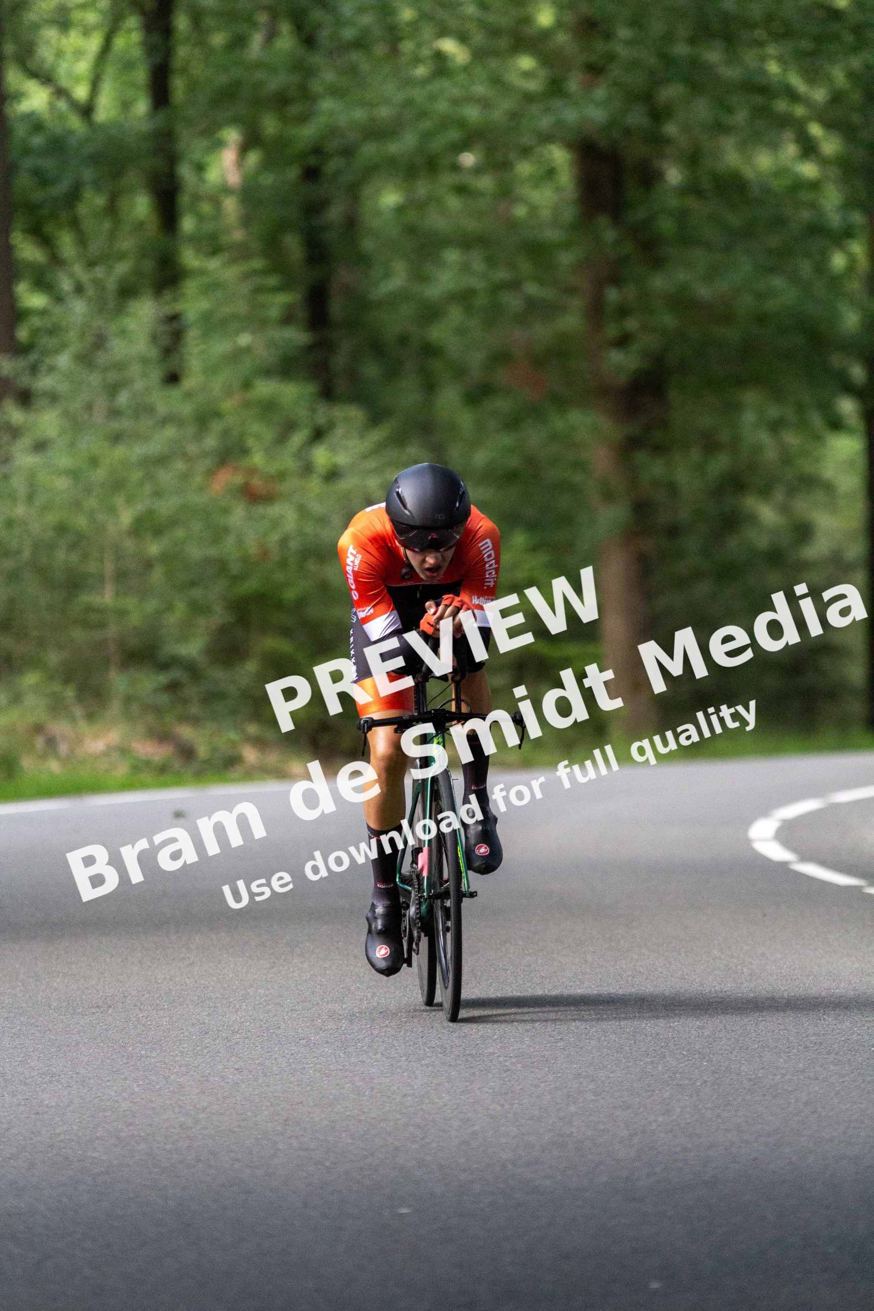 A man in an orange bike racing outfit is riding a bike on the street.