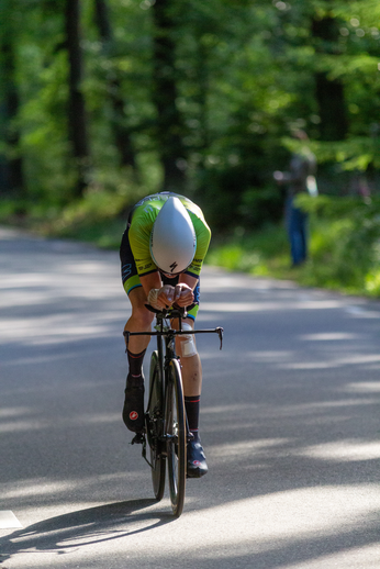 A woman wearing a green and white jersey rides her bike down the road.