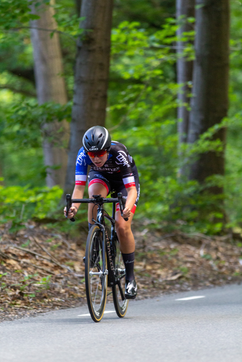 A cyclist on a trail wears a DK helmet and races wearing a blue, white and red outfit.