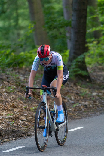 A woman wearing a white and black jersey with blue and yellow accents on the sleeves is riding a blue bicycle.