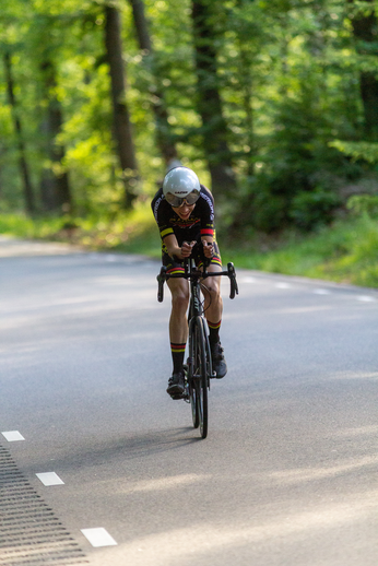 A cyclist wearing a white helmet is riding a bicycle on a road in a forested area.