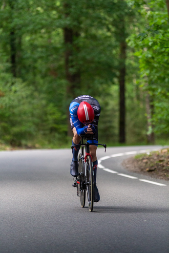 A man wearing a blue shirt and helmet rides his bicycle on the side of a road.